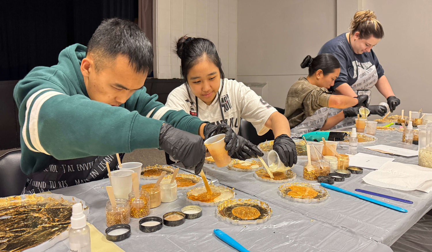 People pouring resin at a table with various items including cups, resin, and supplies.