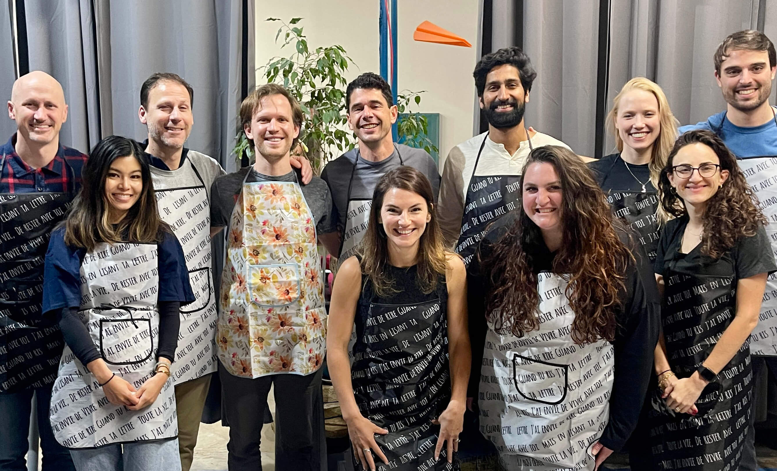 A group of smiling students wearing aprons poses for a group picture after their acrylic pouring team-building workshop.