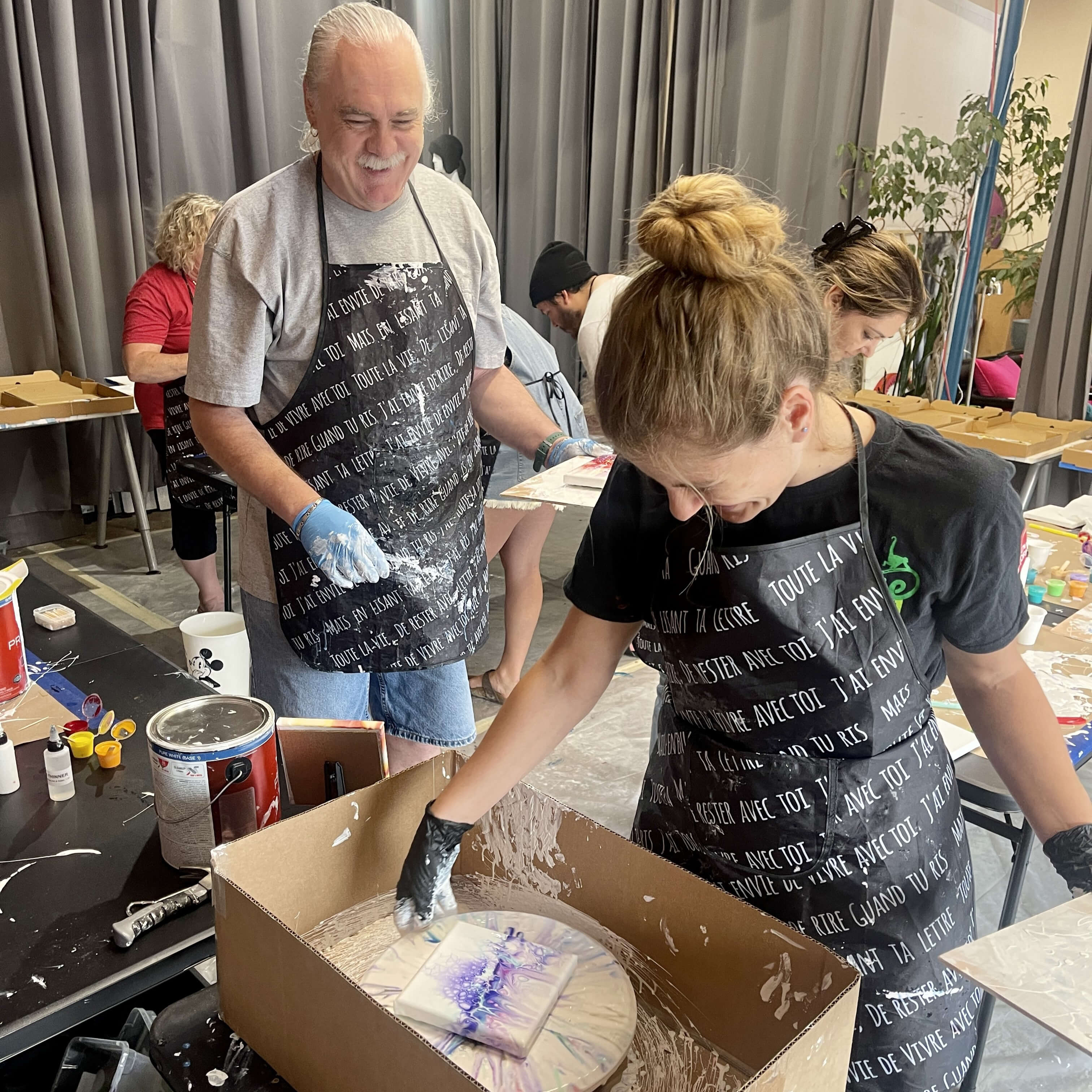 Two happy students interacting during an Acrylic Flow workshop, one using the turning table while the other waits in line.