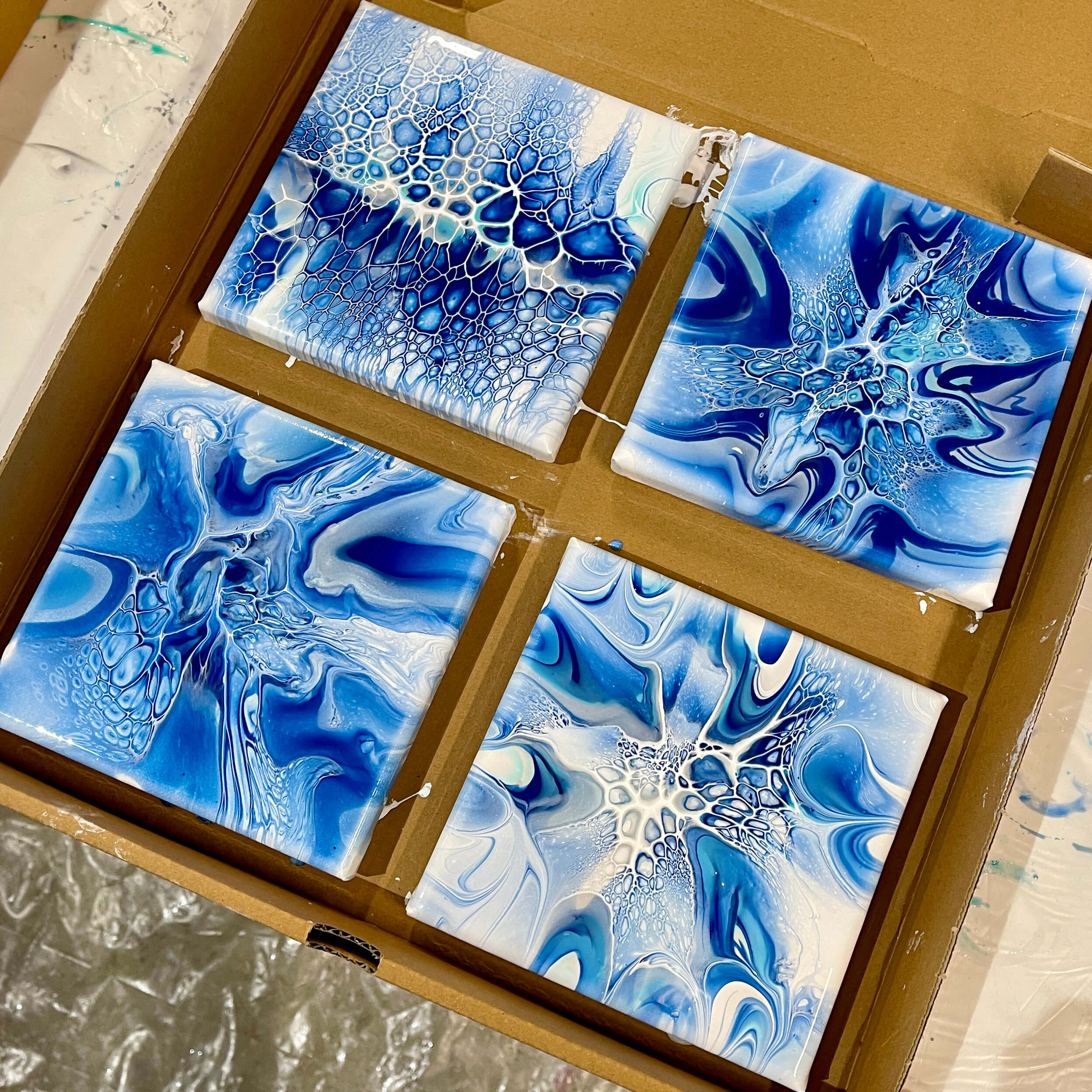 Close-up of four acrylic flow paintings with stunning cells and lacing effects all in a monochromatic blue color scheme.