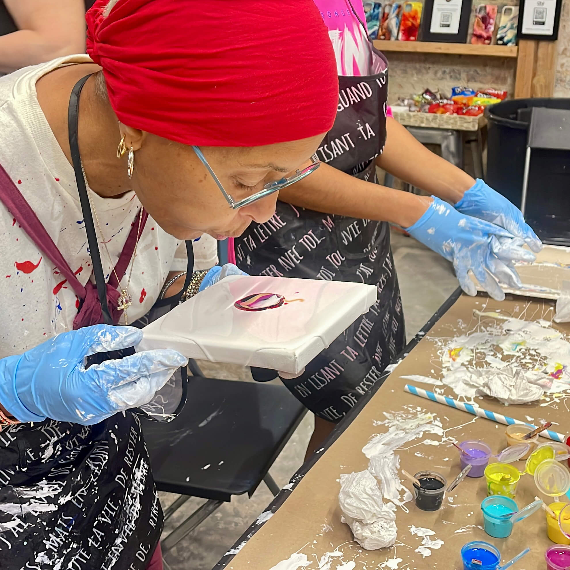 Student in the process of creating her acrylic flow painting by holding the canvas up to her face while blowing onto it.
