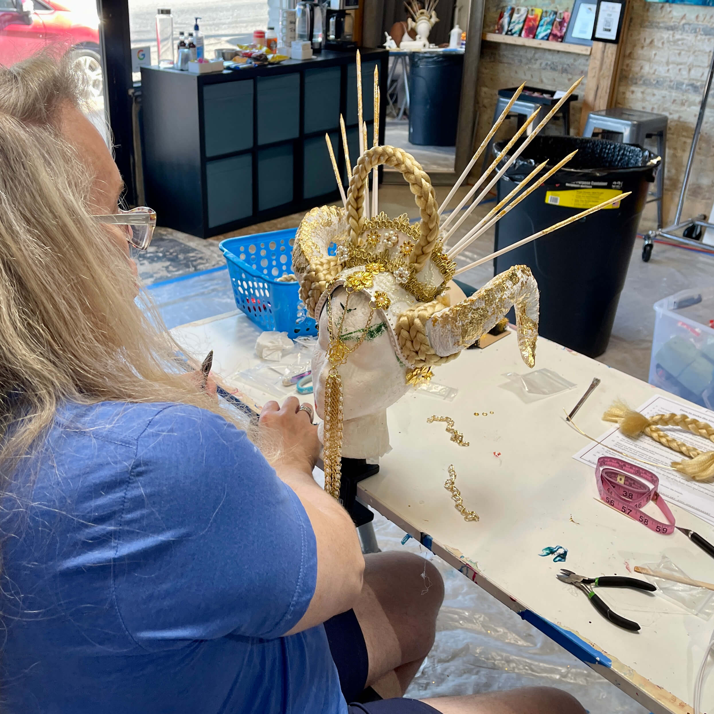 A student attaches gold chains to the front of his gold and white horns headdress creation.