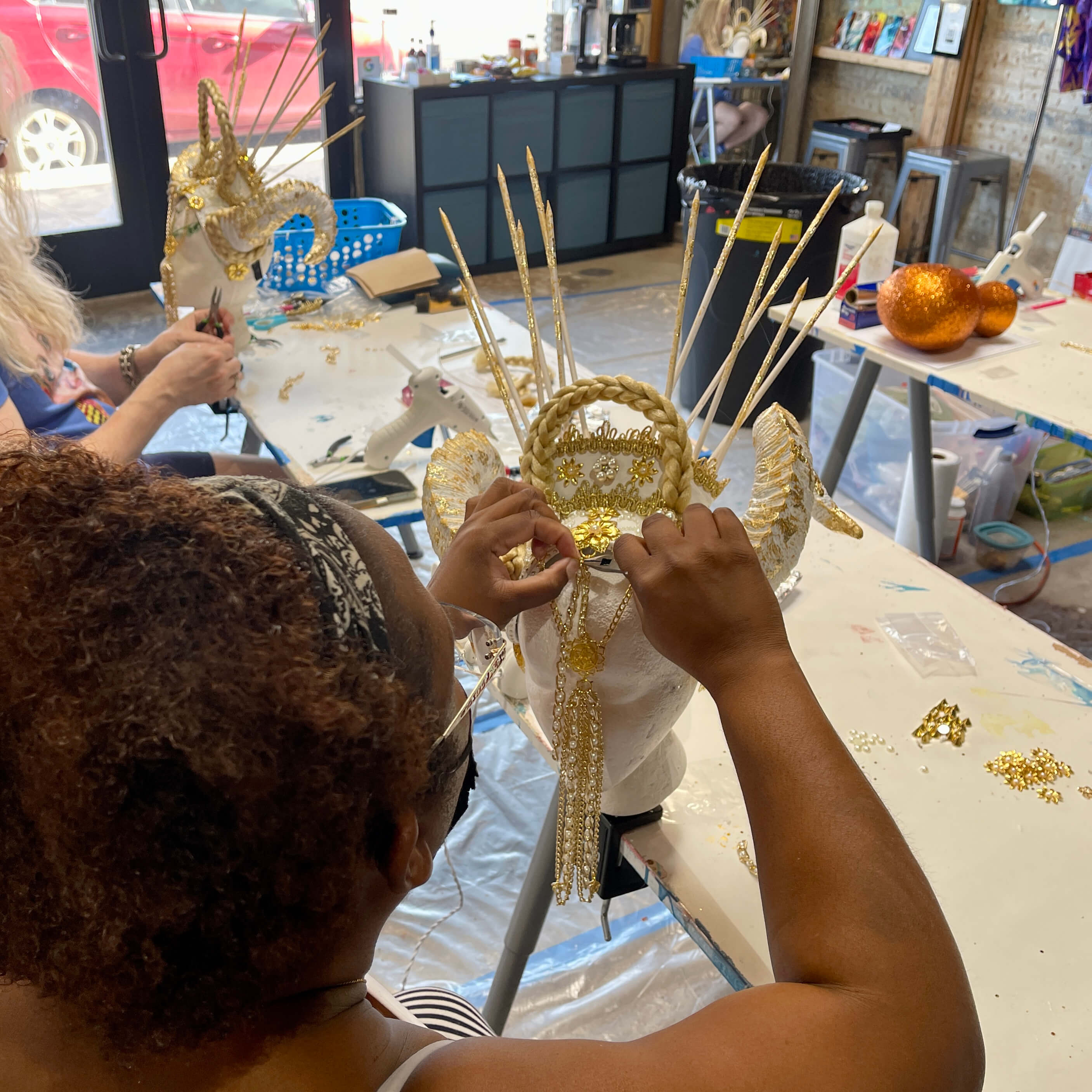 A student secures gold chains to the front of her gold and white horns headpiece during the creation process.