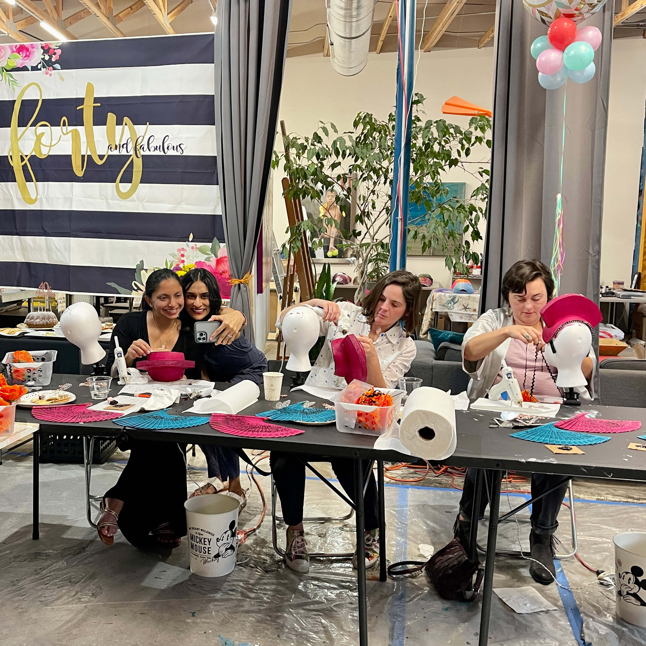 Capturing a moment during a headdress workshop - a couple of guests work on their headpieces while others snap a selfie.