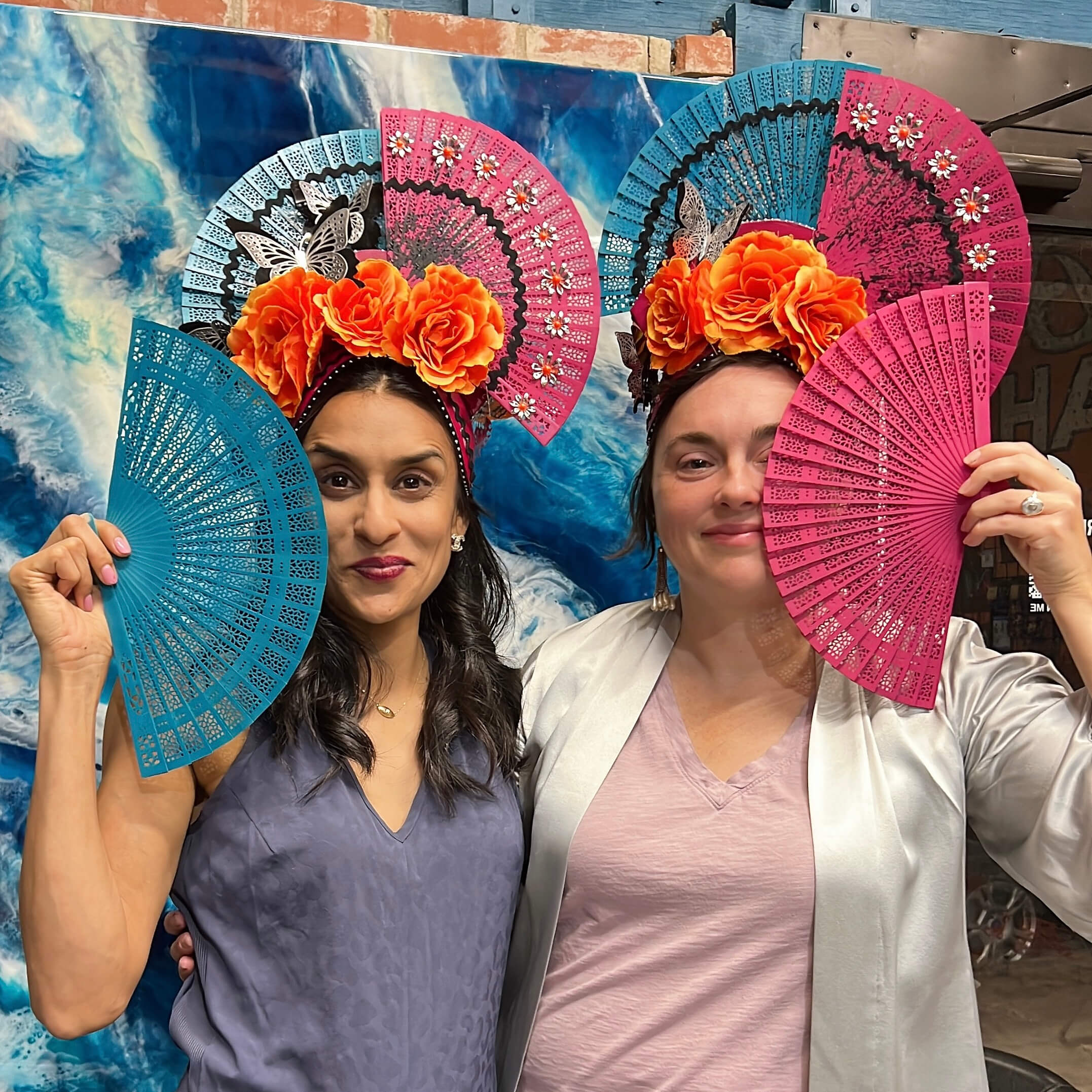 Two headdress workshop participants pose for a fun picture, smiling for the camera while wearing their handmade headpieces.