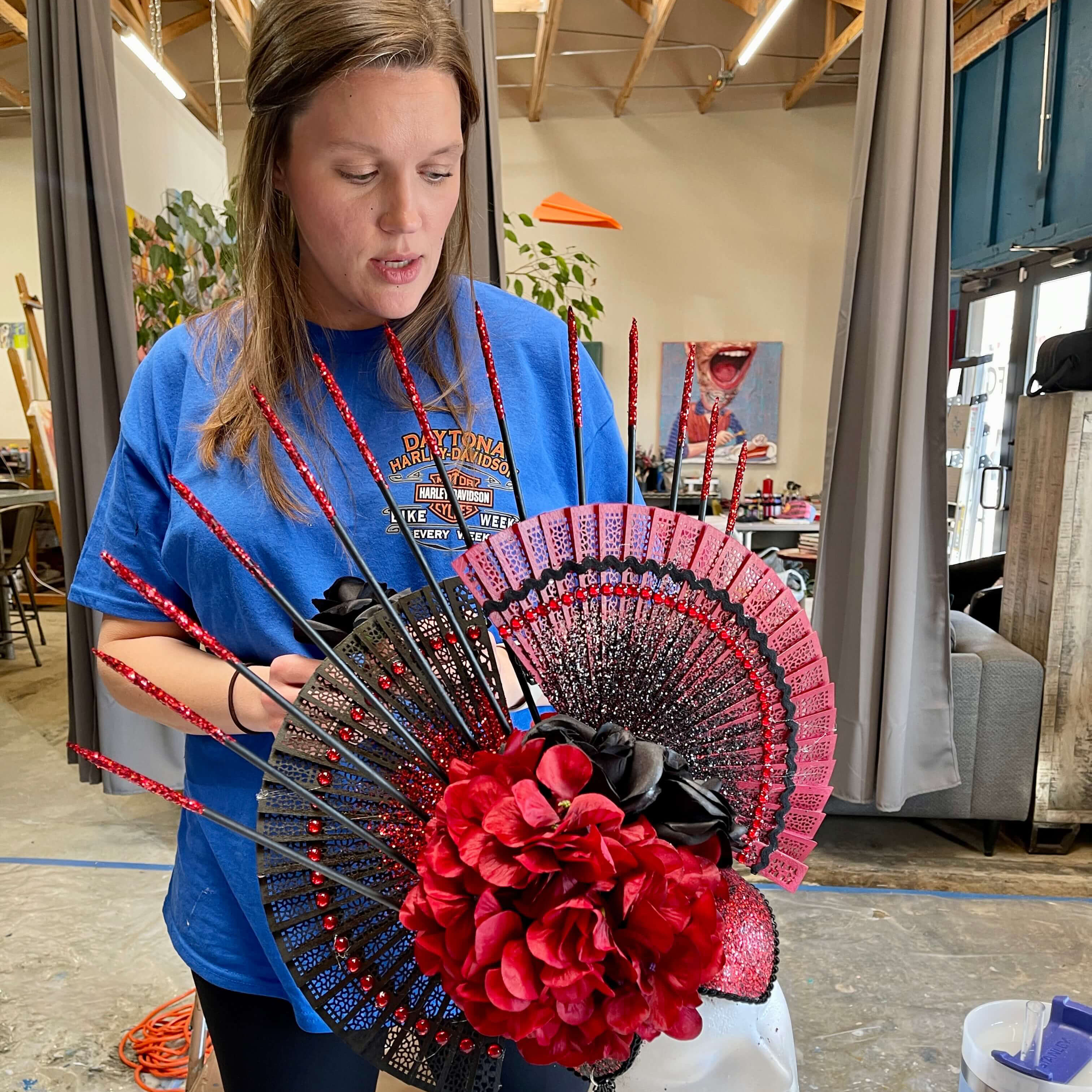 A student places black roses on the backside of her black and burgundy fan and floral headpiece creation.