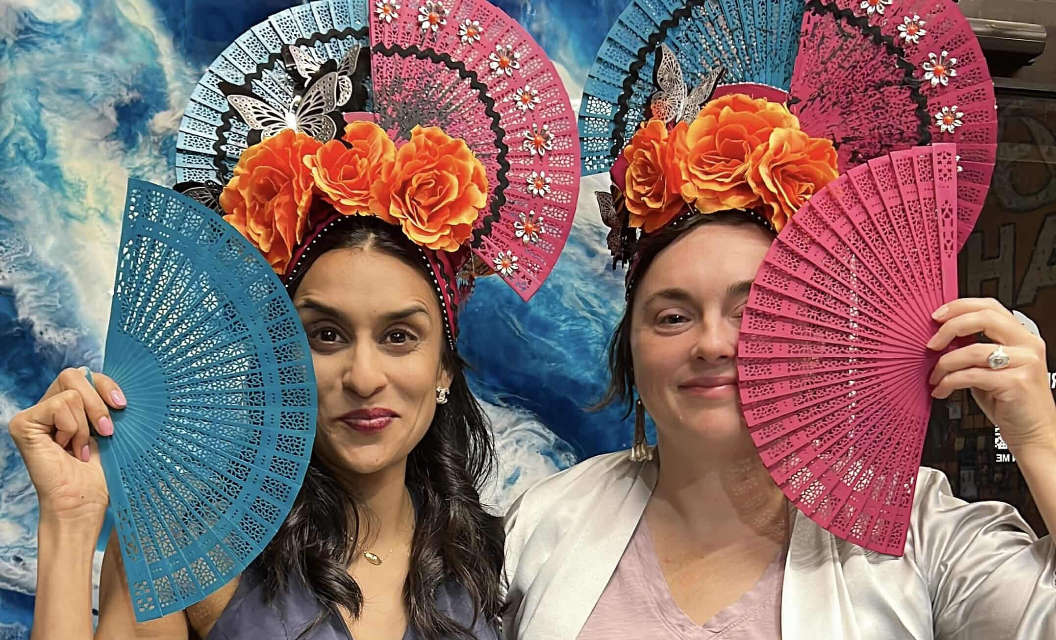 Two headdress workshop participants pose for a fun picture, smiling for the camera while wearing their handmade headpieces.