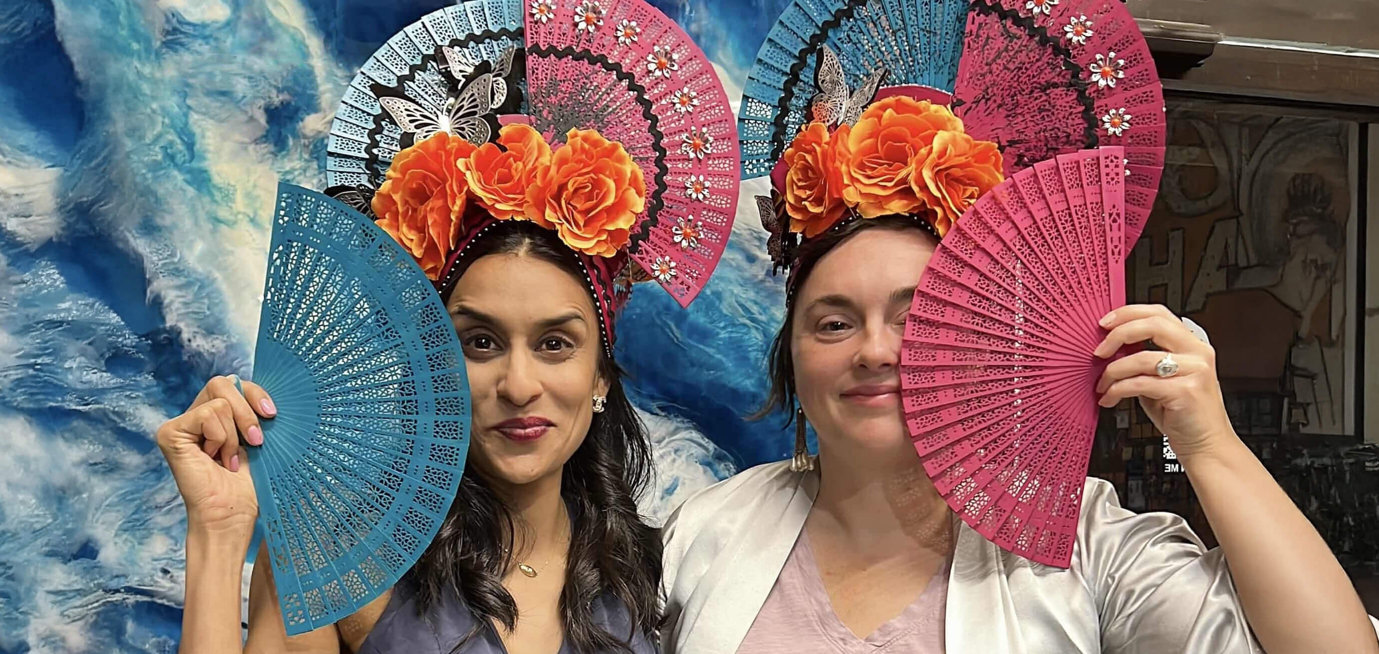 Two headdress workshop participants pose for a fun picture, smiling for the camera while wearing their handmade headpieces.