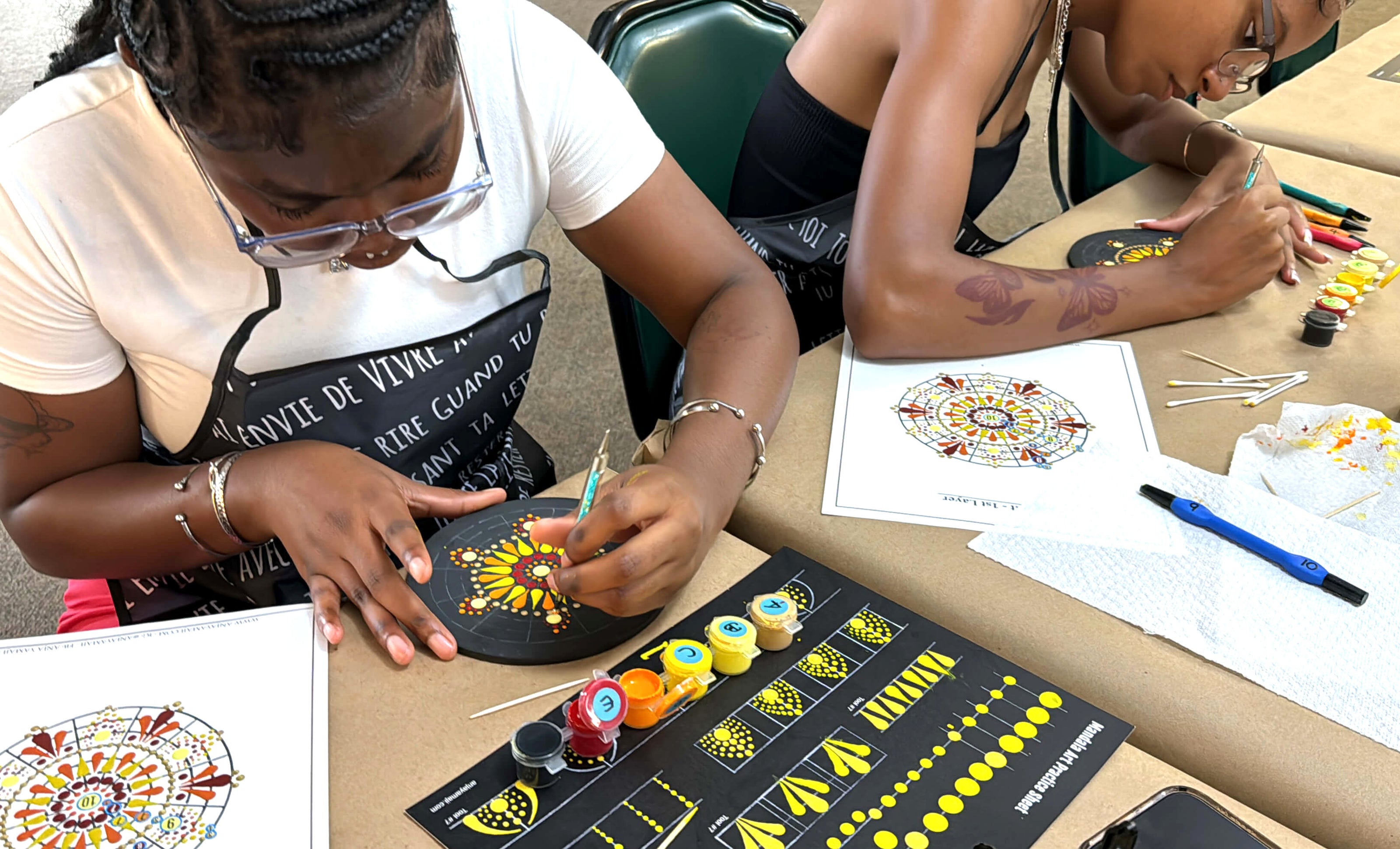 Two mandala art workshop participants focus on painting dots on their wood rounds to create their mandalas.