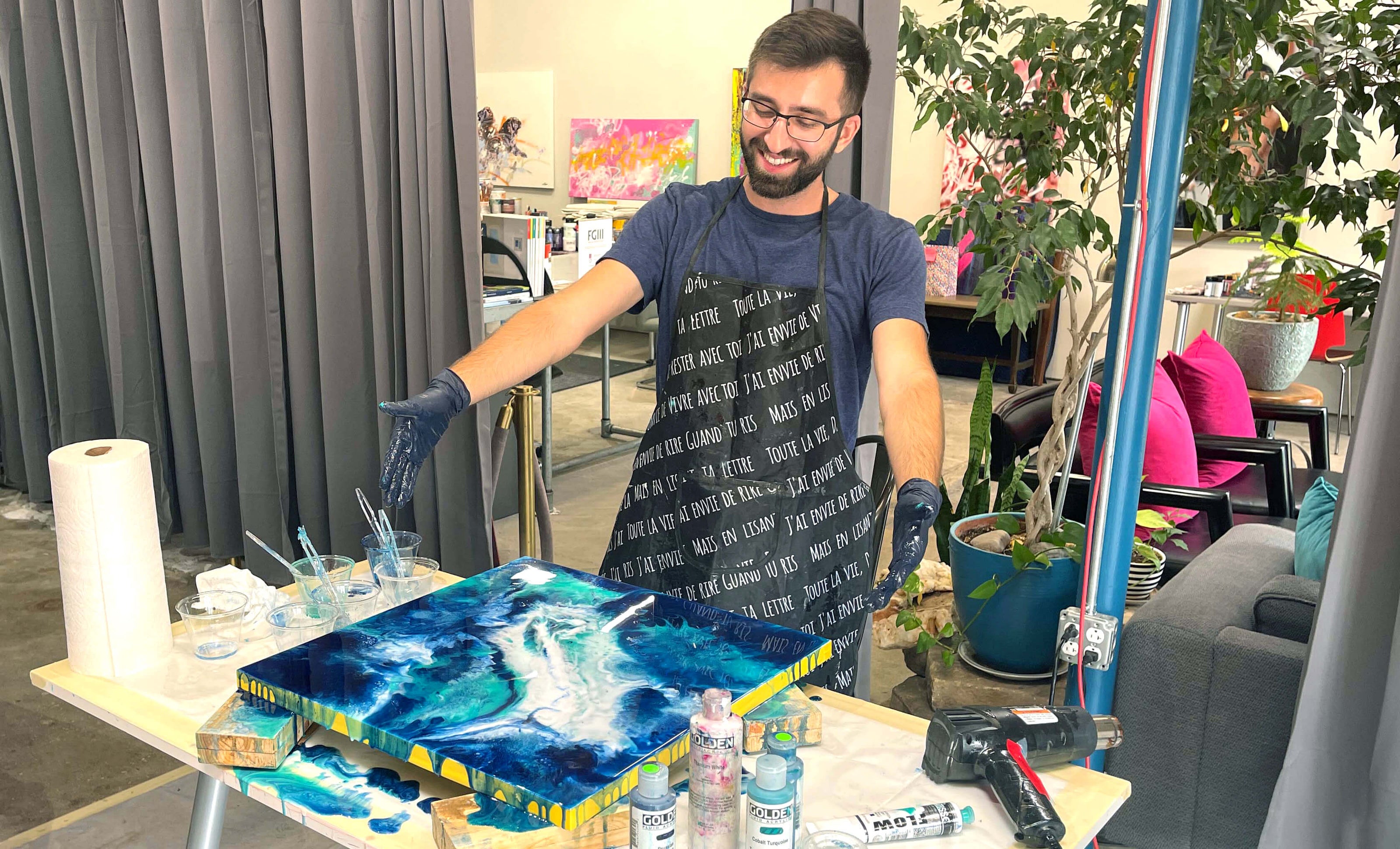 Resin art workshop participant proudly points to his finished blue ocean resin painting while looking at it in front of him.