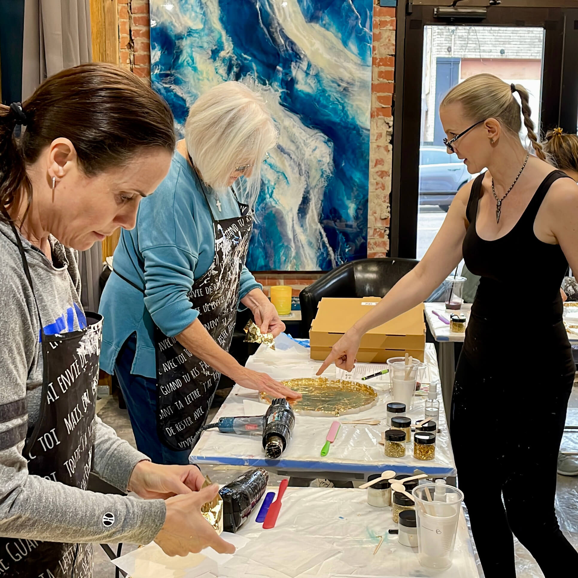 Anja Yamaji points to a student's silicone tray mold, guiding her on how to properly apply the gold leaf sheets.
