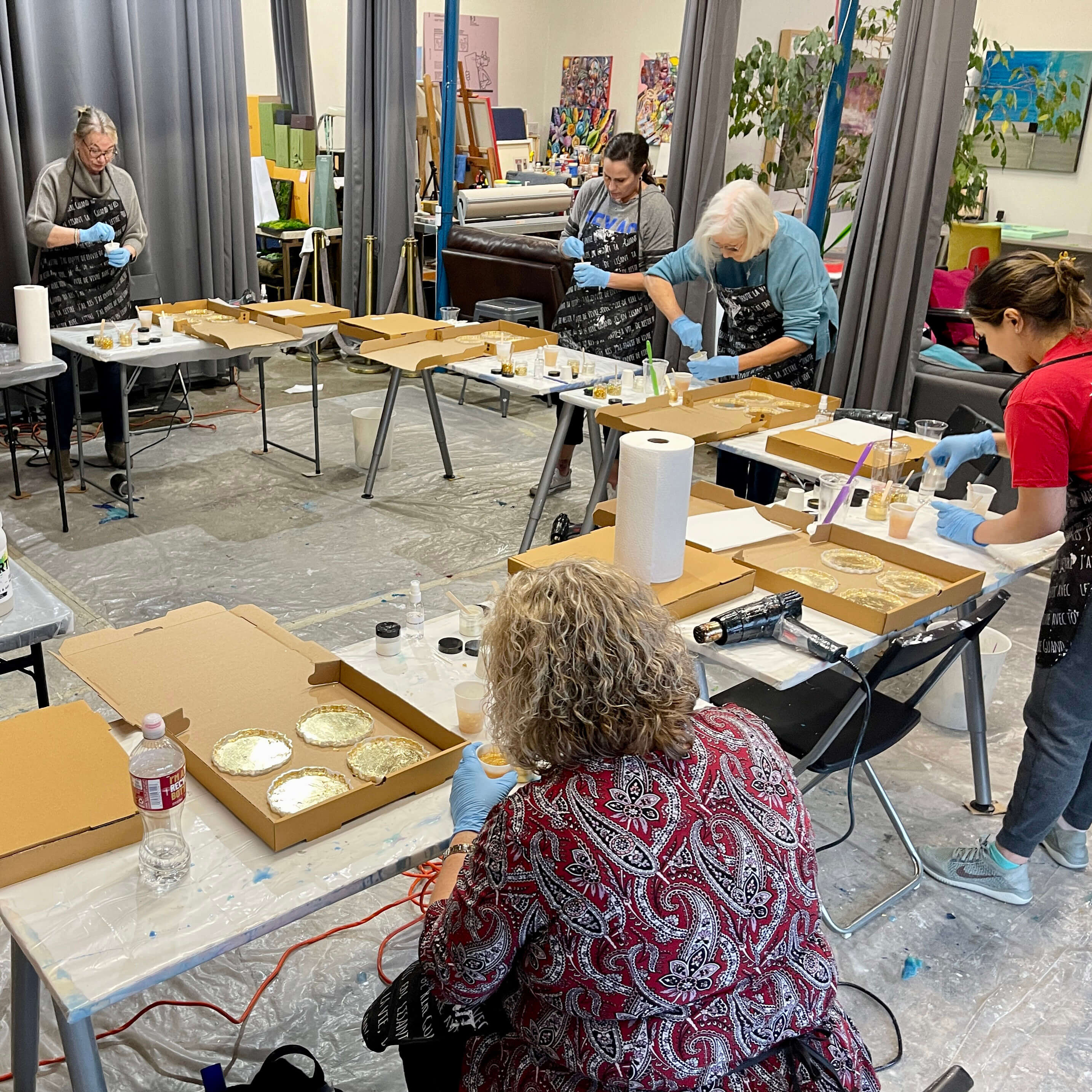 A group of five students mixes different shades of gold pigment into multiple cups filled with clear resin.