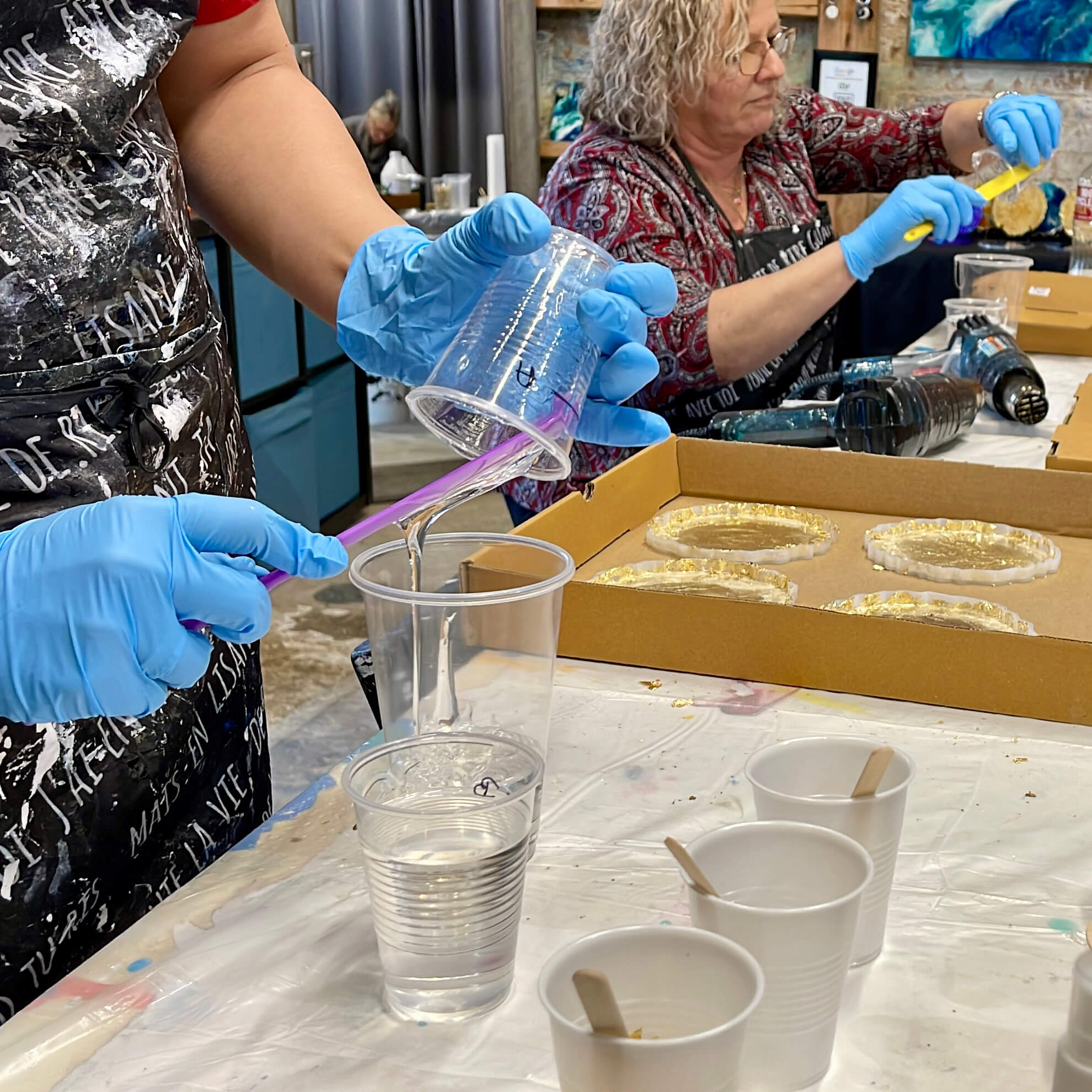 Close-up of a student using a spatula to scrape resin Part A into a larger mixing cup.