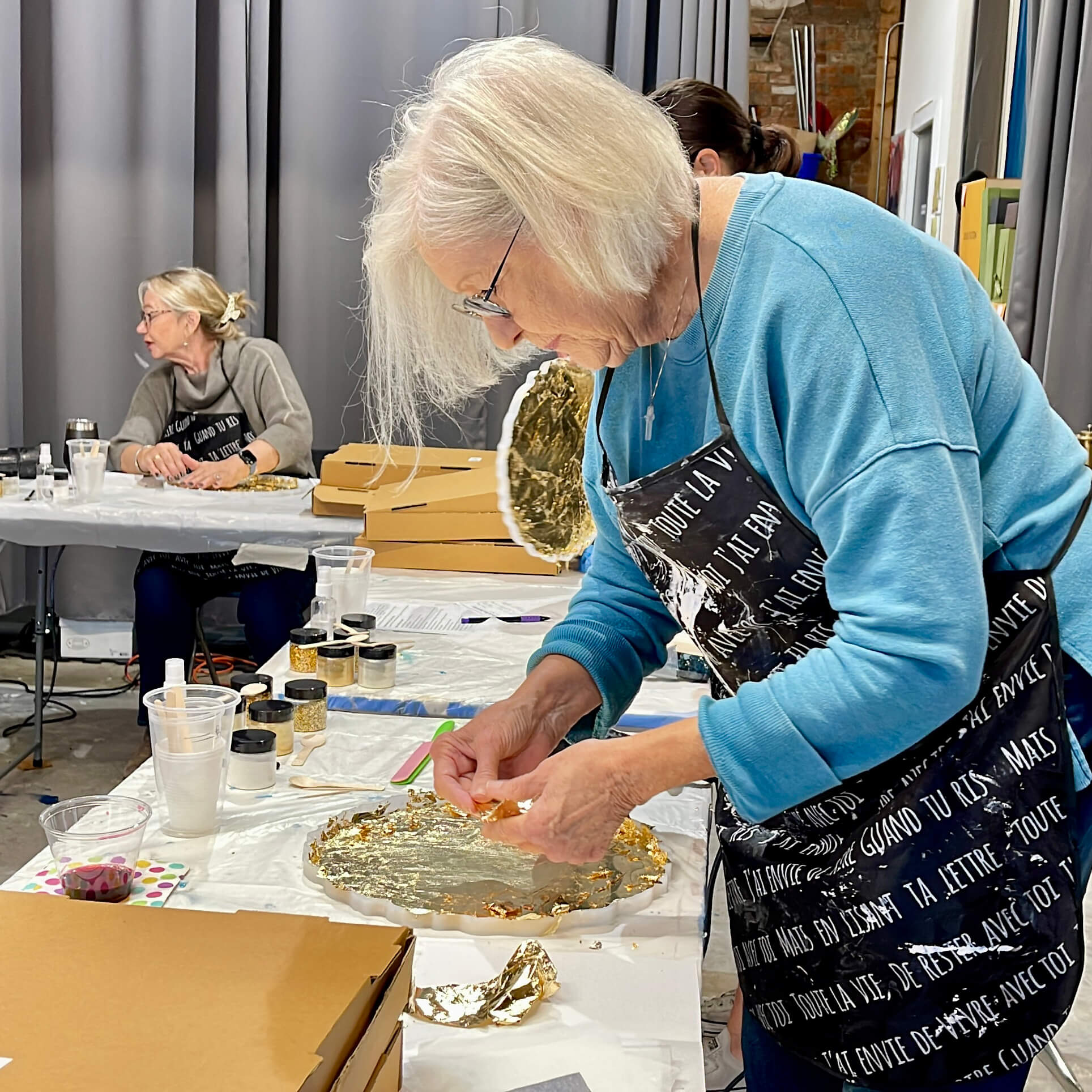 A student prepares her silicone tray mold by applying gold leaf sheets before pouring the resin.