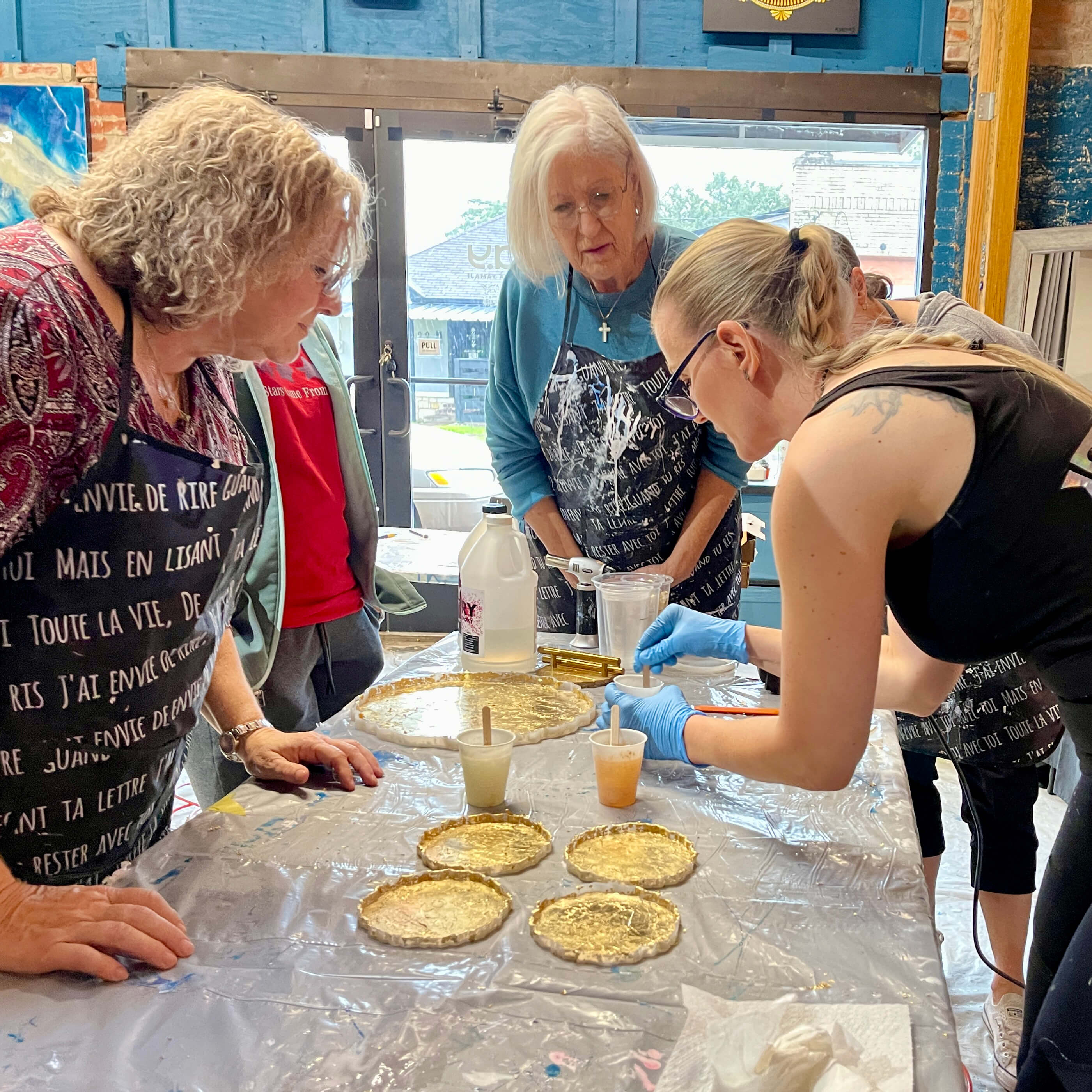 Anja stirs the resin mixture in a cup with a popsicle stick, breaking up the gold leaf as students watch.