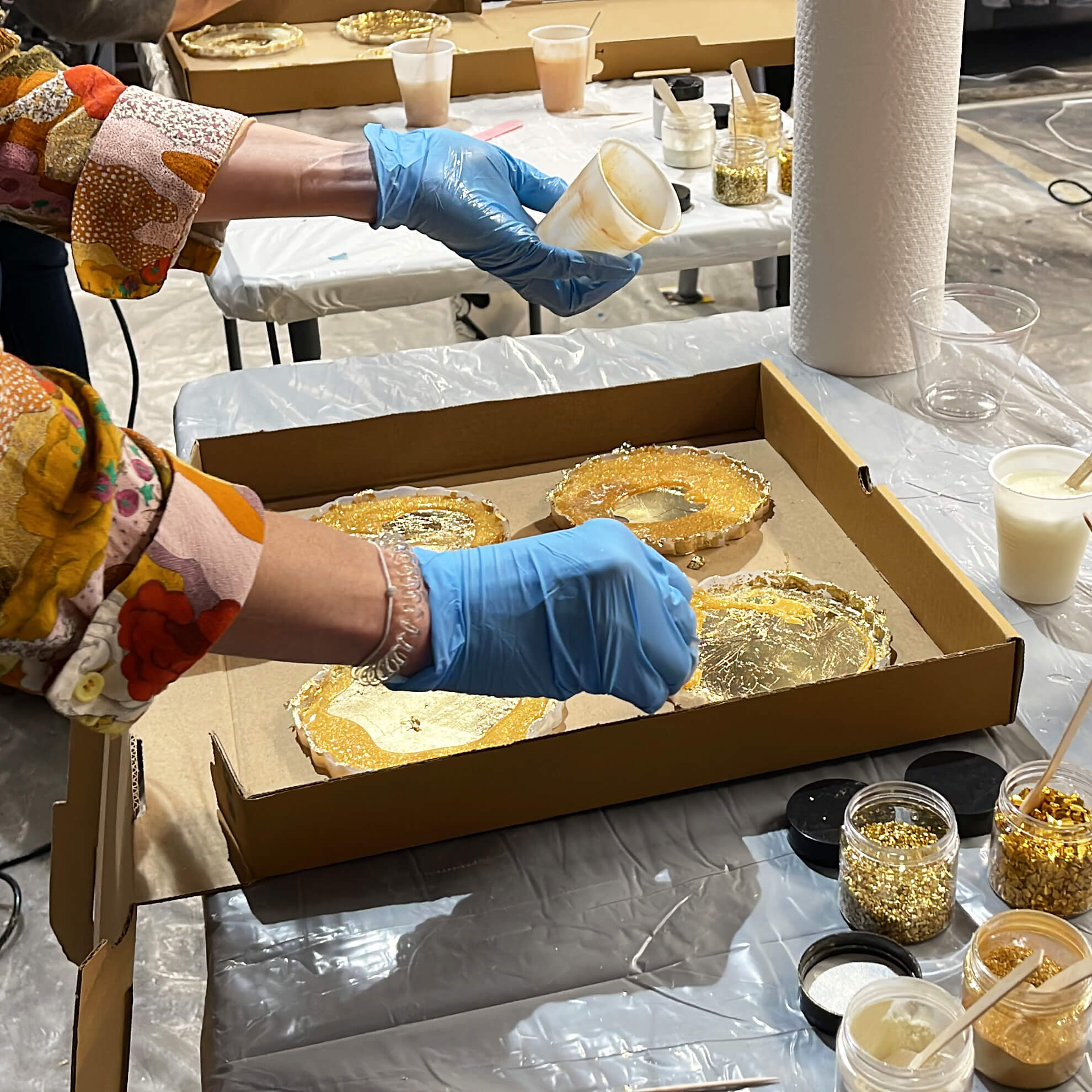 Close-up of a student's workstation as she pours gold resin mixture into her four silicone coaster molds.