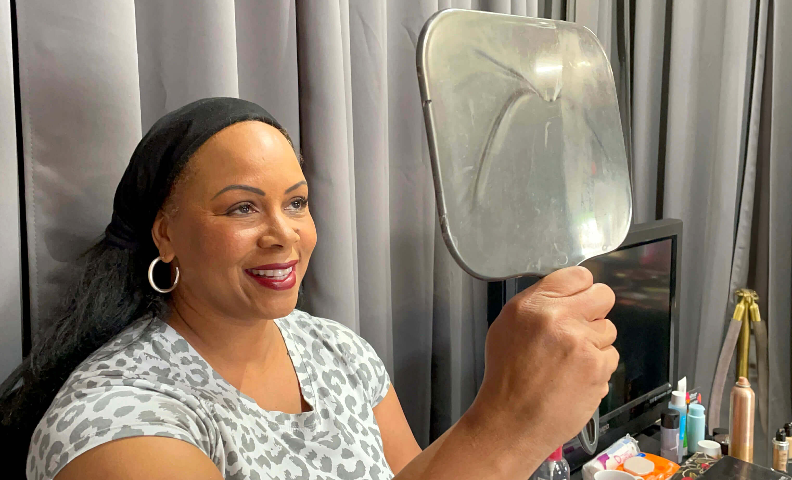 Student holding up a mirror, smiling at her reflection after a beauty makeup experience, happy with her transformation.