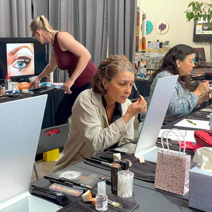 Two workshop participants apply eyeshadow to their faces while Anja Yamaji organizes her workstation.
