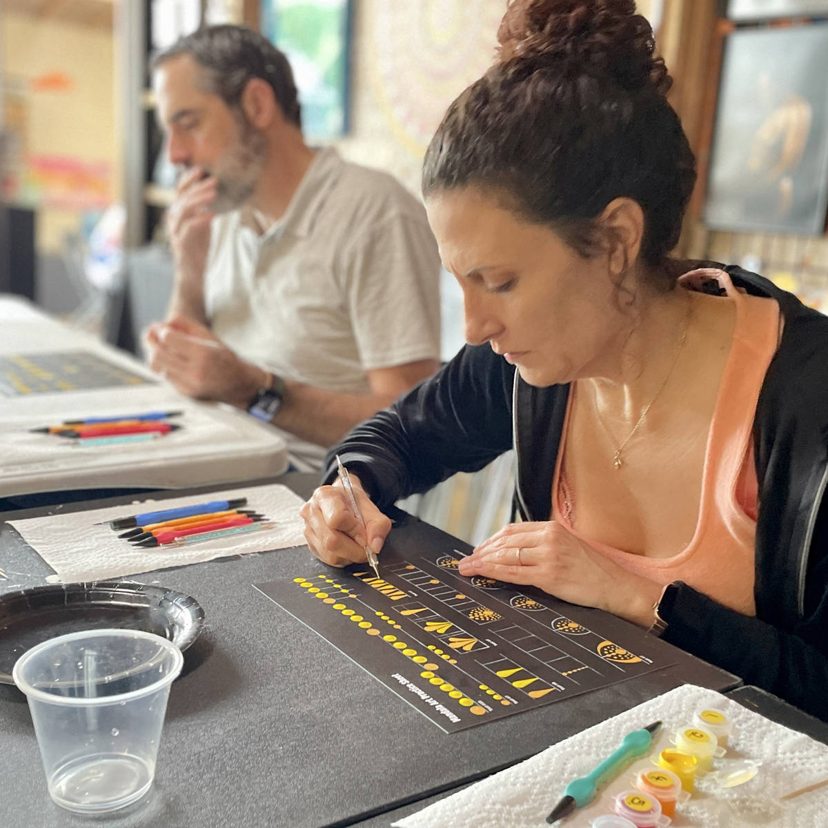 Woman working on her mandala art practice sheet with a man in the background.