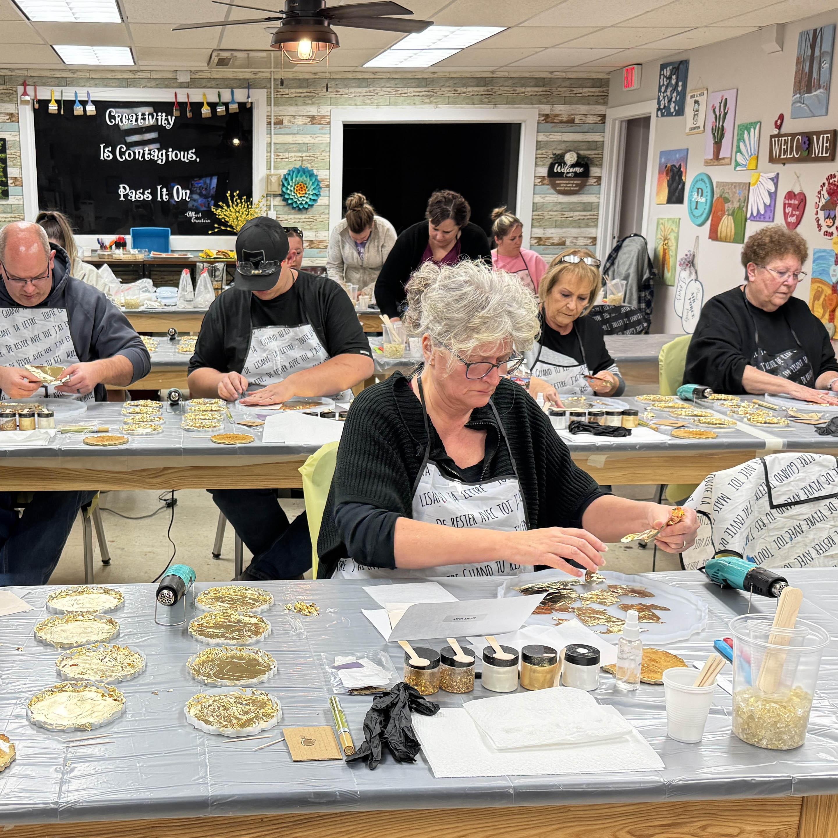 Classroom setting with people working on resin art projects at tables.
